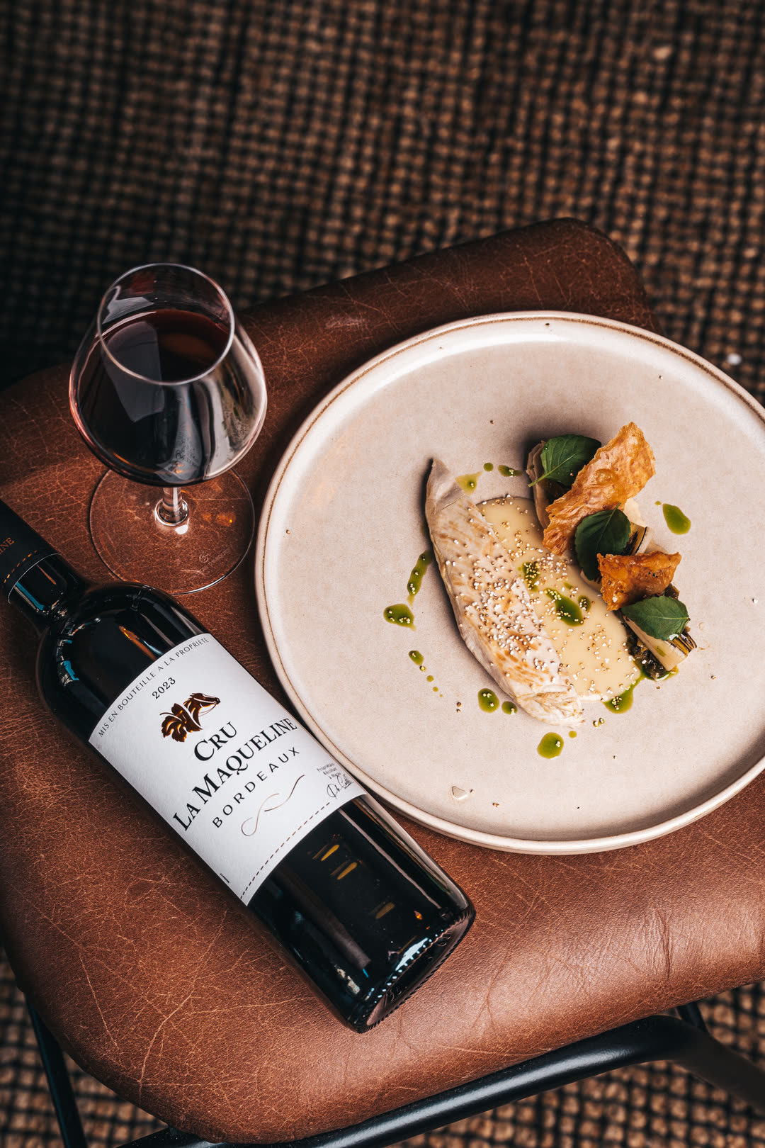 Bouteille de Cru La Maqueline Bordeaux et verre de vin rouge à côté d’une assiette dressée
